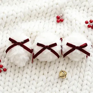 Boules de Noël en peluche blanche avec nœuds en velours bordeaux sur fond tricoté