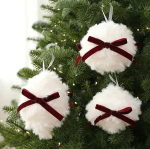 Détail de boules de Noël en fausse fourrure blanche avec nœuds en velours rouge sur sapin