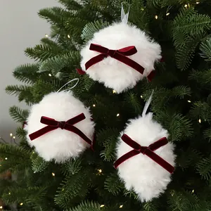 Trois boules de Noël en peluche blanche avec des nœuds en velours rouge sur un sapin