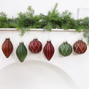 Detail of red and green painted Christmas ornaments hanging on a mantle with greenery
