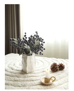 Close-up of artificial blueberry branches in a white textured vase with candle decoration