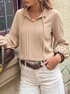 Elegante blusa beige con cuello de volantes, detalles de encaje y diseño plisado.