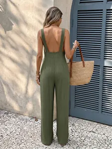 Back view of a woman wearing an olive green backless textured jumpsuit with straw bag