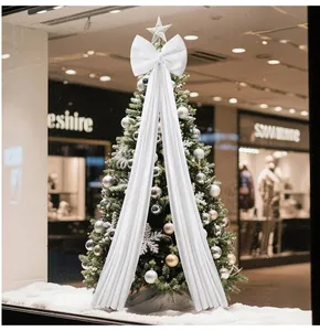 Large white Christmas tree bow ornament hanging on a festive tree in a shop window.