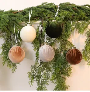 Eleganti palline di Natale in velluto appese a un ramo di pino per decoro festivo.