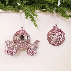 Pink glitter pumpkin carriage and ball Christmas ornaments hanging from pine branch.