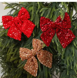 Detail view showing shiny red and gold sequin Christmas bows hanging on a green pine tree