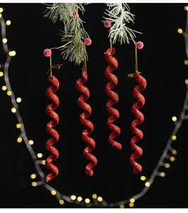 Cuatro adornos navideños en forma de espiral roja con purpurina colgando de pino nevado.