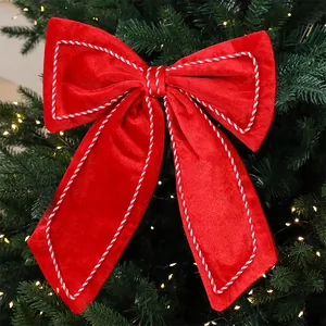 Detail of a large red velvet Christmas bow with white rope trim on a lit pine tree.