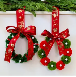 Detalle de dos coronas navideñas hechas a mano con cintas rojas y perlas de imitación.