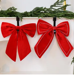 Two large red velvet Christmas bows with white stitching details hanging on fireplace