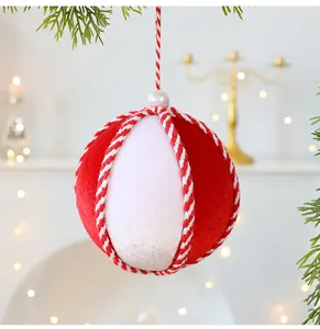Primer plano de una bola de Navidad de terciopelo rojo y blanco de 10 cm colgada de una rama.
