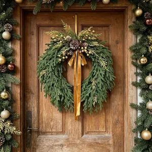 Couronne de Noël luxuriante avec pommes de pin et nœud en velours doré sur porte en bois