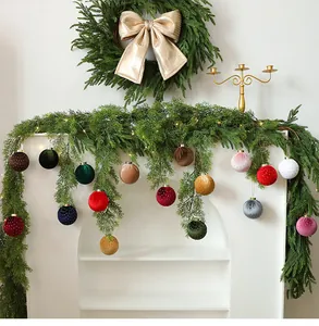 Detalle de bolas de Navidad de terciopelo de colores colgadas de una guirnalda verde