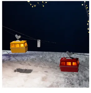 Lit Christmas cable car miniatures on wire over snowy scene for festive holiday decor