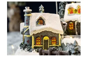 Detailed close-up view of a resin Christmas village house featuring snow texture and warm lights.