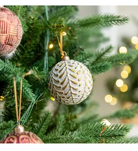 Detailed view of white and gold textured Christmas ball hanging on tree with lights