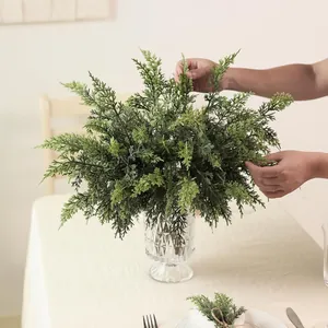 Handen die kunstmatige ceder takken in een kristallen vaas schikken voor decor