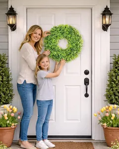 Realistic artificial boxwood wreath being hung on a white front door as decoration