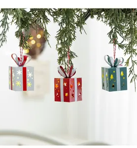 Trois ornements de boîtes-cadeaux en métal lumineux suspendus à des branches de Noël