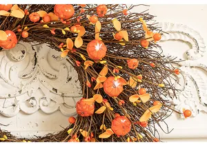 Close-up detail of a handmade autumn harvest wreath featuring small pumpkins and berries.