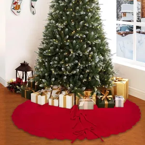 Détail d'un grand tapis de sapin de Noël rouge tricoté placé sous un arbre festif.