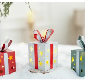 Détail de trois mini ornements de boîte cadeau lumineux en fer dans un décor de neige