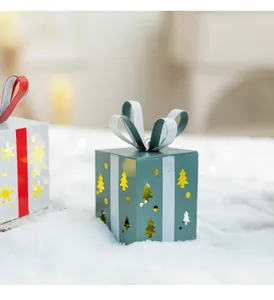 Détail d'une boîte cadeau de Noël en métal sarcelle avec des découpes d'arbres sur neige