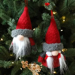 Paire de nains de Noël en peluche faits main suspendus à un sapin de Noël festif et illuminé