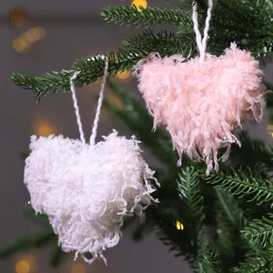 Suaves adornos navideños de corazón esponjosos blancos y rosas colgados en una rama.