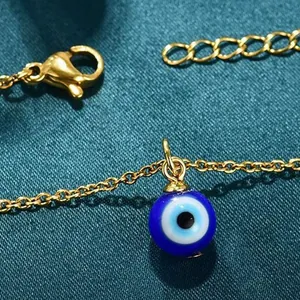 Close-up detail of a blue glass evil eye pendant on a delicate gold-toned chain.