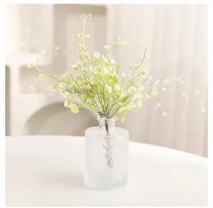 Close-up of elegant artificial green foliage in a textured glass vase for home decor.