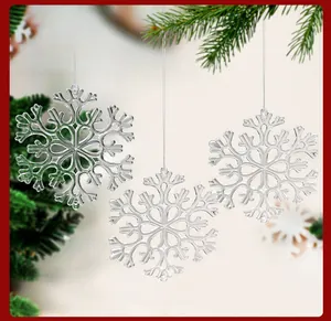 Gros plan de trois flocons de neige en plastique cristallin suspendus à des branches de pin.