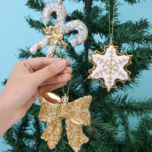 Glittering gold bow Christmas tree hanging ornament held against a festive green tree