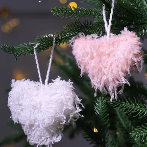 Pink and white fluffy heart feather ornaments hanging on a festive Christmas tree branch