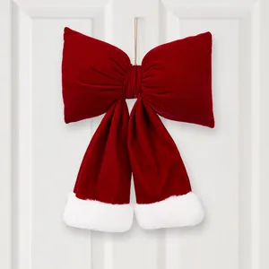 Large red velvet Christmas bow with white fur trim hanging on a white door for holiday home decoration