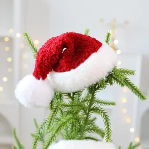Decoratieve zachte rode en witte kerstmuts van pluche bovenop een groene kerstboomtak