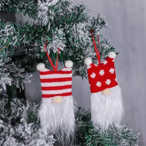 Pair of red and white Christmas gnome ornaments hanging on a snowy pine tree branch.