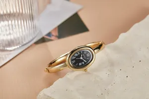Close-up van een vintage goudkleurig armbandhorloge met een ovale zwarte wijzerplaat.