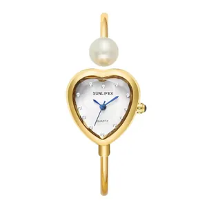 Reloj brazalete dorado con forma de corazón para mujer con detalle de perla y agujas azules