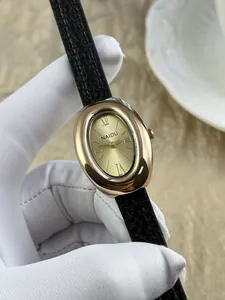 Detailweergave van een vintage gouden dameshorloge met zwarte leren band en NAIDU-wijzerplaat