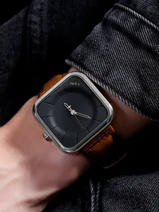 Primer plano del reloj cuadrado TOMI con esfera negra y correa de cuero marrón en la muñeca