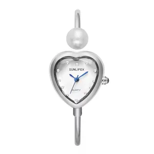 Vista detallada del reloj brazalete corazón plateado con perla y marcadores de cristal