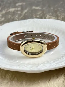 Detail van een vintage ovaal goudkleurig dameshorloge met bruine leren band op een bord