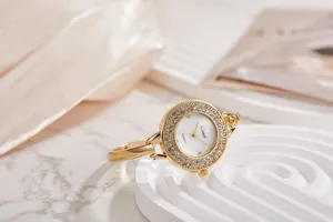 Dettaglio di un elegante orologio a bracciale da donna in oro con lunetta di strass e quadrante bianco