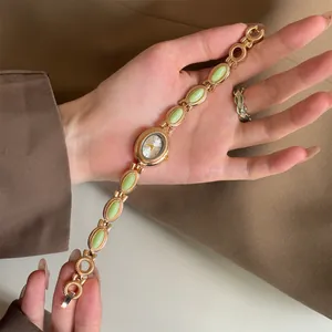 Détail d'une montre-bracelet dorée vintage avec d'élégantes incrustations de pierres vertes.