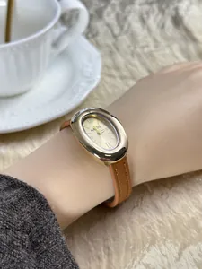 Detailopname van een vintage ovaal gouden horloge met bruine leren band om een pols
