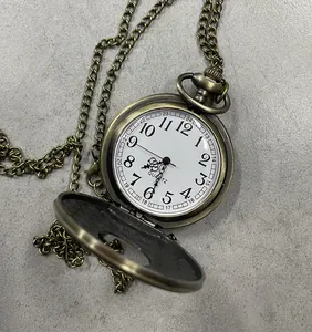 Vista detallada de un reloj de bolsillo vintage de bronce con esfera blanca y cadena larga.