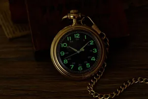 Détail macro d'une montre de poche vintage dorée avec cadran vert lumineux dans le noir