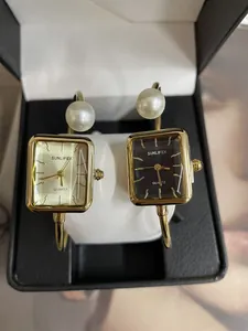 Dettaglio ravvicinato di eleganti orologi quadrati dorati con bracciali di perle e quarzo